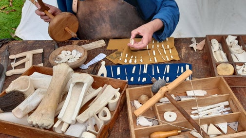 A table of animal bones and antlers with a craftsperson using traditional techniques to make Roman-style hairpins and jewellery